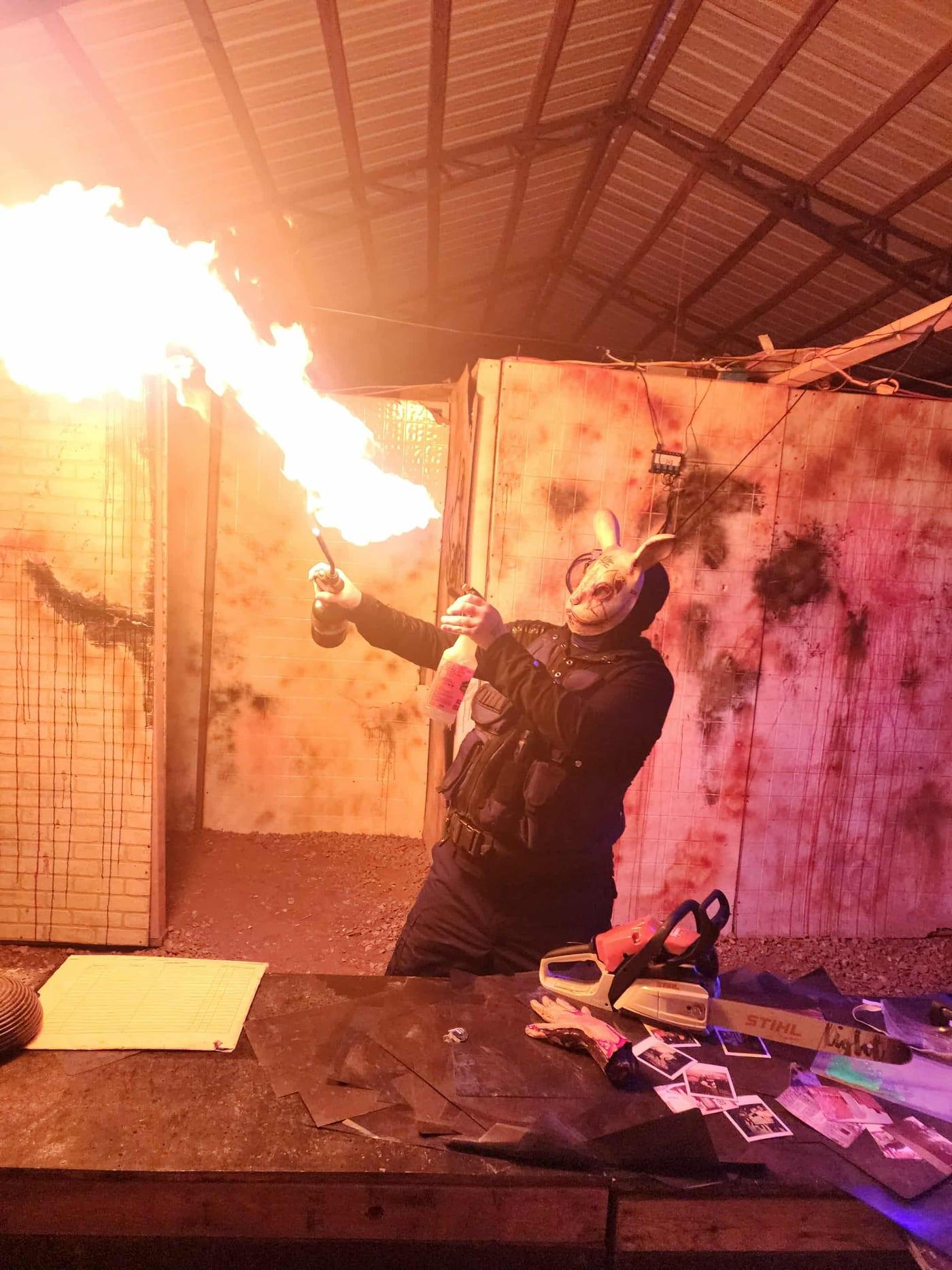 A performer with a flame prop against a distressed wall